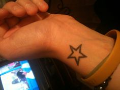 a person's wrist with a star tattoo on it and a television in the background