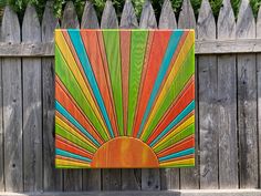 an art piece is displayed in front of a wooden fence, with the sun painted on it