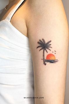 a woman's arm with a small palm tree and sunset tattoo on the left upper arm