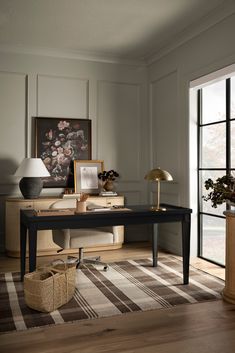 a room with a desk, lamp and pictures on the wall next to a large window