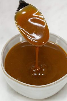 a spoon full of caramel sauce in a white bowl