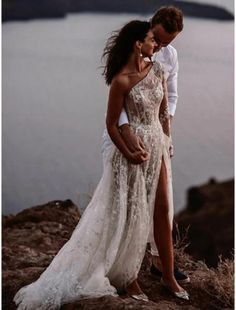 a man and woman standing next to each other on top of a hill near the ocean