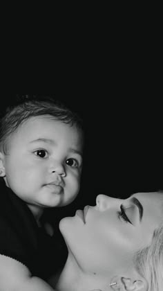 a black and white photo of a woman holding a baby in her lap, with the child's face partially obscured by it