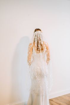 a woman in a wedding dress is standing against a wall with her veil over her head