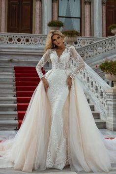 a woman standing in front of stairs wearing a wedding dress