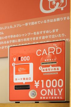 an orange card machine sitting on top of a wooden shelf next to a sign that says card