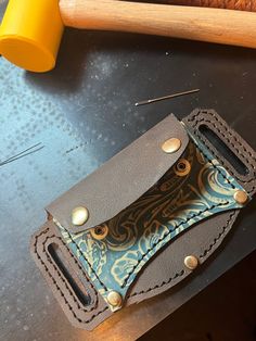 a leather wallet sitting on top of a table next to a hammer and some wood