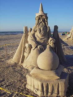 a sand sculpture on the beach with a wizard sitting in it's lap and holding a ball