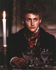 a man sitting at a table with wine glasses in front of him and a lit candle behind him