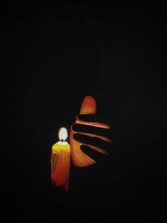 a lit candle sitting on top of a table next to an orange object in the dark