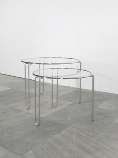 two circular glass tables sitting on top of a floor next to each other in front of a white wall