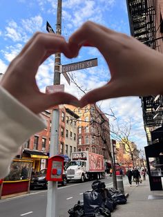 a person making a heart shape with their hand on the corner of an urban street