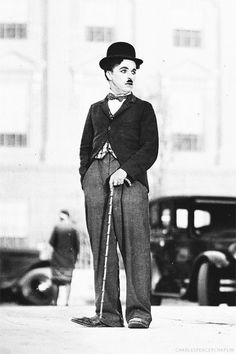 an old black and white photo of a man in top hat with cane standing on sidewalk