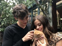 a young man and woman holding an orange cat