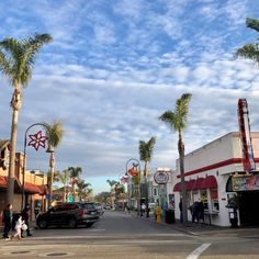 people are walking down the street in front of shops and palm trees on a cloudy day