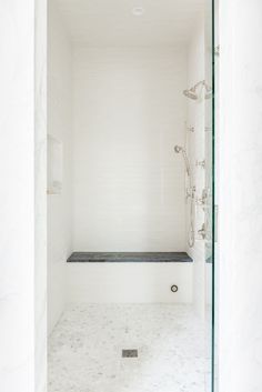 a white bathroom with marble flooring and glass shower enclosures, along with a walk in shower