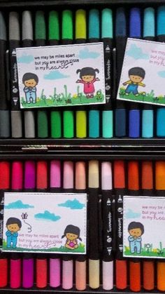 two rows of crayon markers with children's drawings on them in the background