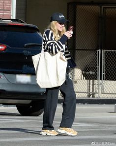 a woman in black and white striped shirt holding a cell phone while standing next to a car