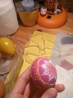 a hand is holding an egg in front of some other eggs on a table with candles