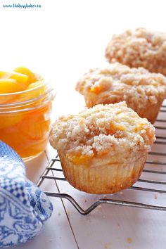 three muffins sitting on a cooling rack next to some oranges and jam