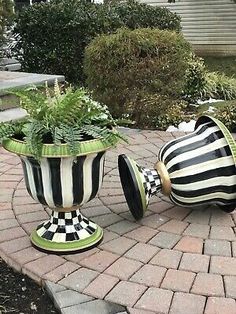 two black and white striped vases sitting on top of a brick walkway next to plants