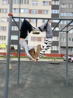 two young boys are playing on the swings in an empty parking lot with apartment buildings in the background