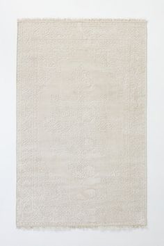 a white rug with an intricate design on the front and back side, against a white wall