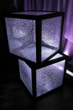 a lit up cube sitting on top of a wooden table next to a purple curtain