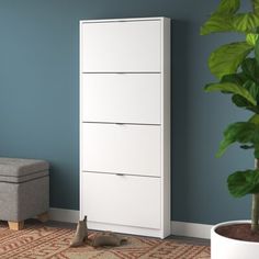 a white chest of drawers next to a plant in a living room with blue walls