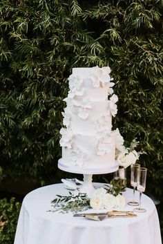 a white wedding cake sitting on top of a table next to wine glasses and flowers