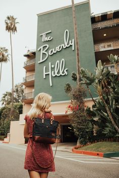 a woman in a red dress is walking towards the beverly hills sign and palm trees