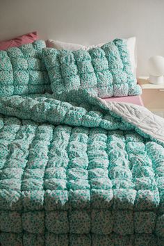 a bed with green and white bedspread, pillows and blankets on top of it