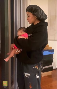 a woman holding a baby in her arms while standing next to a glass door and looking into the room