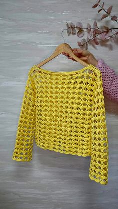 a yellow crocheted sweater hanging on a wooden hanger next to a plant