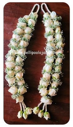 white roses and baby's breath flowers are arranged on a wooden table with beads