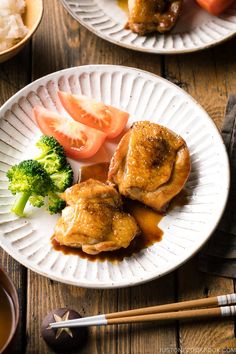 two white plates with chicken, tomatoes and broccoli on them next to chopsticks