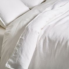 an unmade bed with white sheets and pillows