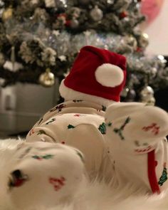 a baby laying in front of a christmas tree wearing a santa hat and leg warmers