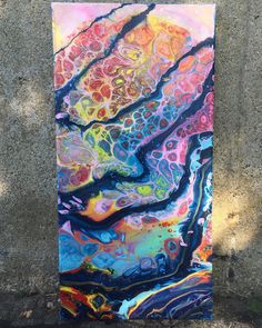 an abstract painting is hanging on the side of a concrete wall in front of a tree