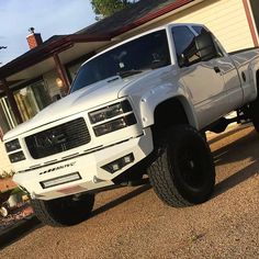 a white truck is parked in front of a house with black tires and rims