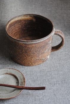 a brown cup and saucer sitting on top of a gray cloth covered tablecloth