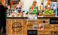 a woman standing in front of a food stand filled with fruits and veggies