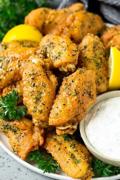 a white plate topped with chicken wings and lemon wedges next to a bowl of ranch dressing