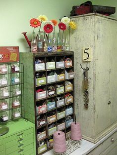 an old cabinet with lots of bottles and flowers in it next to a green dresser