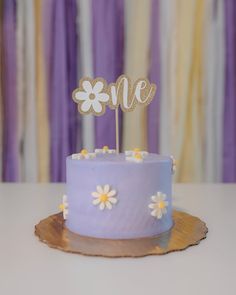 a blue cake with white flowers on top and the word me spelled out in gold