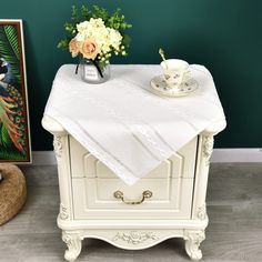 a white table with flowers and a tea cup on it in front of a green wall