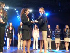 two women shaking hands on stage with other people