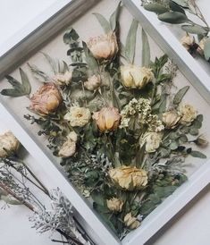 an arrangement of flowers is displayed in a white frame on the wall next to other floral arrangements