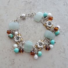 Mixed beading elements are linked in this floral beaded silver bracelet. Wire wrapped aventurine beads are accented with dangles of turquoise magnesite beads, white freshwater cultured pearl beads and amber glass beads.  A playful and colorful bracelet that gives a tropical beach vibe to the mix of elements.  Bracelet has a magnetic closure.  Magnetic closures make for easy open close feature and fit on the bracelet, but they are magnetic.   if you prefer a lobster claw closure on this bracelet I will be happy to make the substitution.  Just let me know with your order and I will make the change. The bracelet measures 7". If you need additional links for a different fit just send me a message with your order. All of my jewelry items come boxed and lace ribbon tied and tagged.  This bracele Bohemian Pearl Bracelet With Spacer Beads For Jewelry Making, Pearl Bead Bracelet, Linked Bracelet, Green Beaded Bracelets, Colorful Bracelet, Bracelets Design, Turquoise Bead Bracelet, Beads Bracelet Design, Silver Bead Bracelet