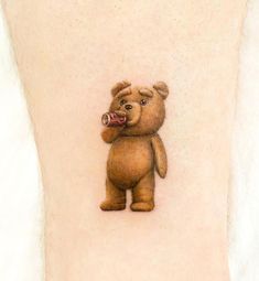 a small tattoo of a teddy bear holding a beer in it's mouth, on the ankle